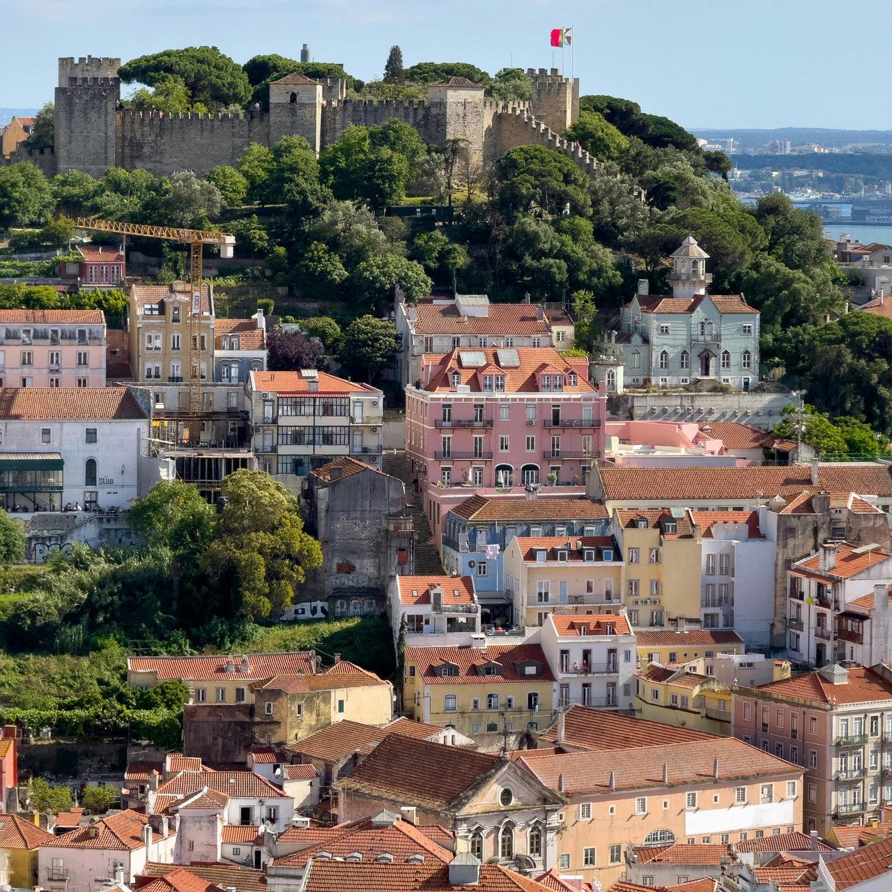 Panoramic view of Lisbon, Portugal, featuring São Jorge Castle atop a hill overlooking a vibrant historic cityscape of colorful buildings with traditional terracotta roofs.