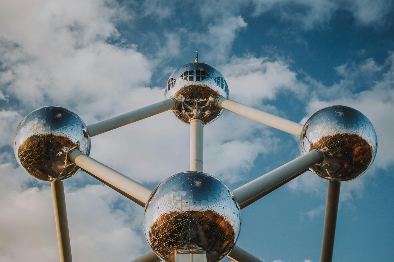 Iconic Atomium monument in Brussels, Belgium, featuring its shiny metallic spheres reflecting the sky and landscape, set against a blue sky with white clouds.