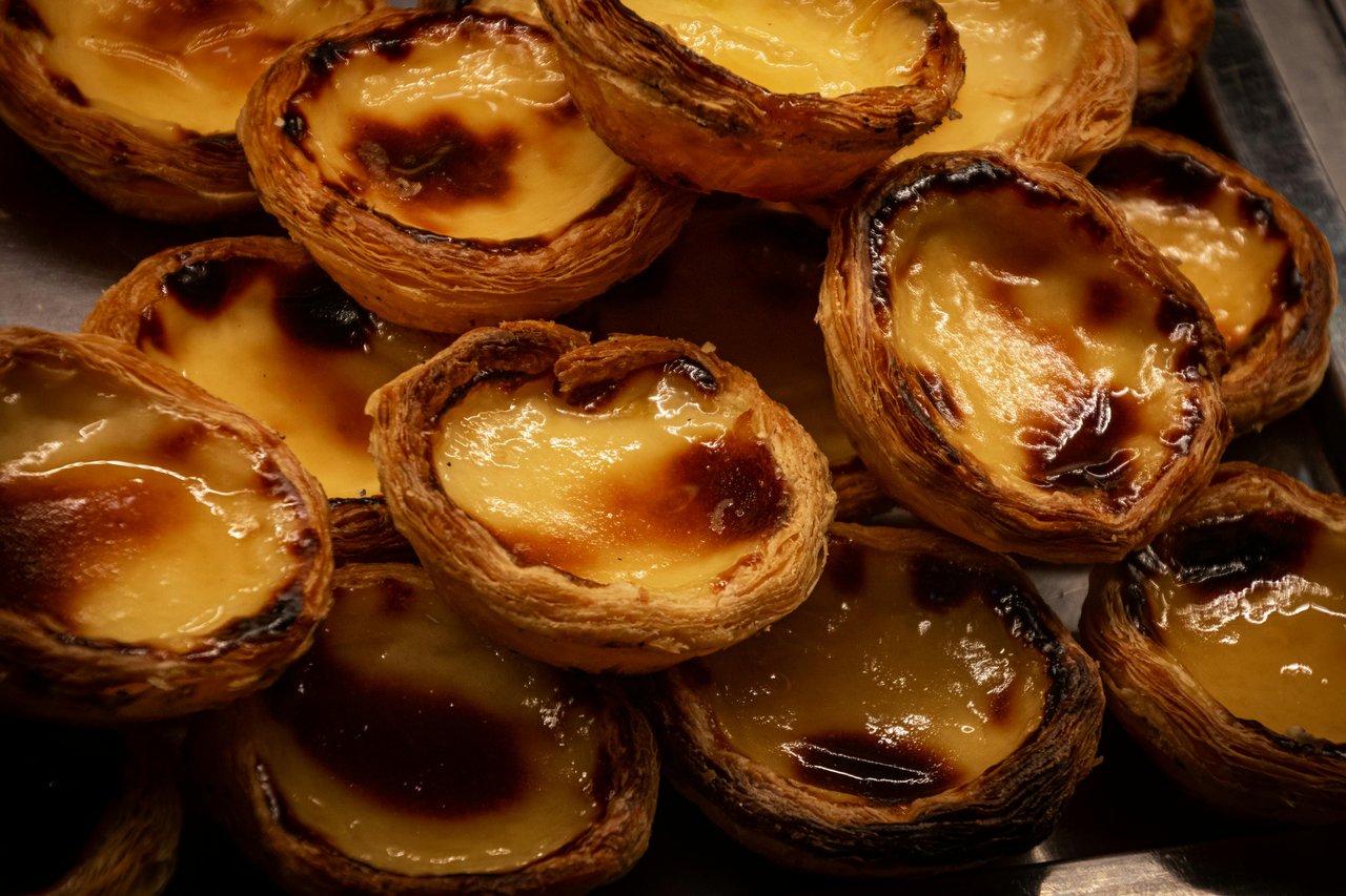 Close-up of a cluster of freshly baked Portuguese Pastéis de Nata. Each traditional egg tart features a flaky, golden-brown crust and a rich, creamy, caramelized custard filling, a quintessential treat from Portugal.
