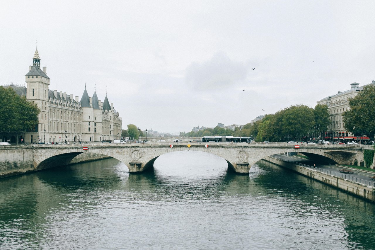 Pont au Change bridge over the Seine River in Paris, featuring the historic Conciergerie building on Île de la Cité on a cloudy day.