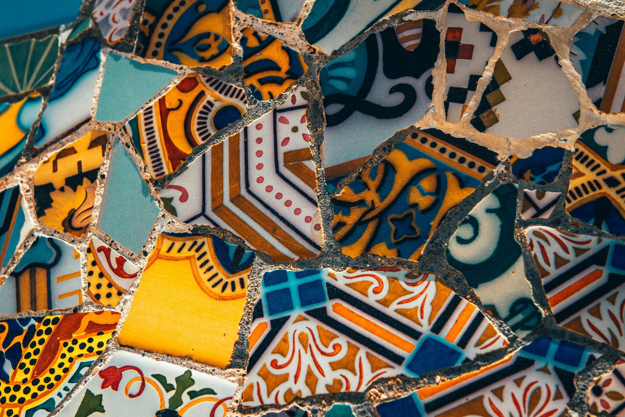Close-up of a vibrant trencadís mosaic from Park Güell, Barcelona, featuring intricate patterns on broken ceramic tiles in shades of blue, yellow, orange, and white.