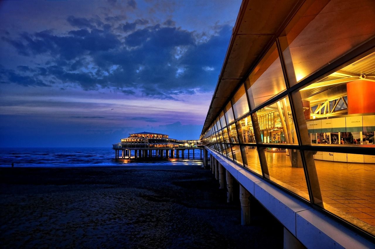 Illuminated Scheveningen Pier and modern architectural promenade at dusk, with the North Sea and dark sand beach in The Hague, Netherlands.