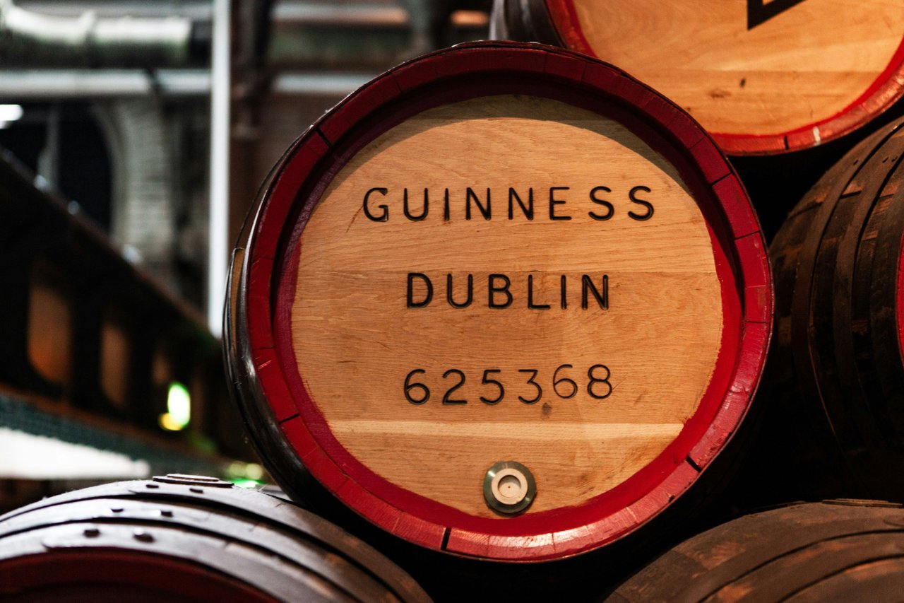 Wooden Guinness beer barrels stacked in a Dublin brewery, with 'GUINNESS DUBLIN' clearly visible on the end of a barrel.