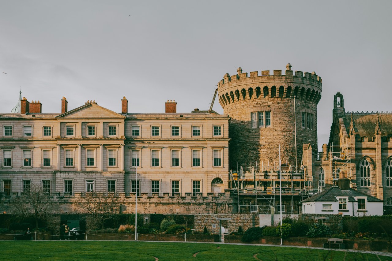 Historic Dublin Castle in Ireland, showcasing the stone Record Tower, the classical State Apartments, and the Gothic Chapel Royal under a bright sky with a green lawn.