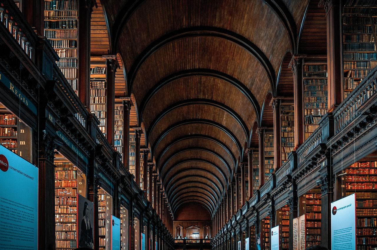 The iconic Long Room library at Trinity College Dublin, Ireland, showcasing its historic architecture with towering dark wood bookshelves, arched wooden ceilings, and antique books.