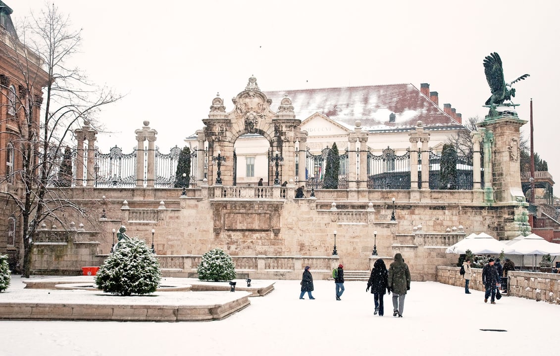 Snowy winter view of the historic Buda Castle in Budapest, Hungary, featuring the iconic Turul bird statue and ornate Habsburg Gate.