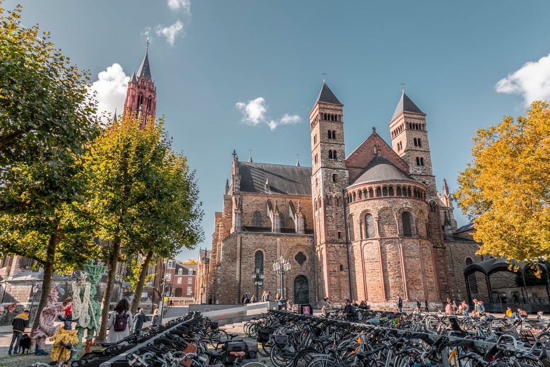 Maastricht, Netherlands: The historic Basilica of Saint Servatius and Saint John's Church at Vrijthof square, with rows of parked bicycles in the foreground on a sunny day.