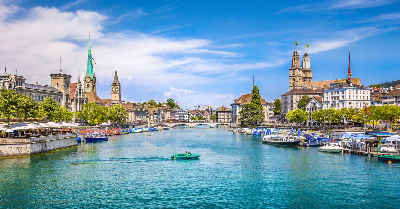 Vibrant panoramic view of Zurich, Switzerland, showcasing the turquoise Limmat River, historic city center, iconic Grossmünster and Fraumünster churches, bridges, and boats on a sunny day.
