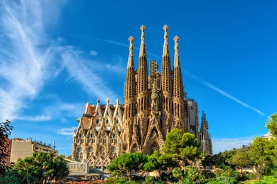 The iconic Sagrada Familia basilica in Barcelona, Spain, featuring its intricate Gothic and Art Nouveau spires against a bright blue sky.