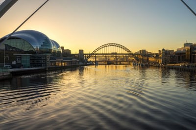 Golden hour view of the River Tyne in NewcastleGateshead, featuring the Sage Gateshead building and the iconic Tyne Bridge at sunset.
