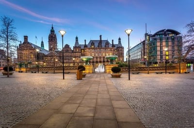 Dusk cityscape of Sheffield, UK, featuring the grand, illuminated Sheffield Town Hall, the Peace Gardens with fountains, and the modern easyHotel Sheffield building under a blue sky.